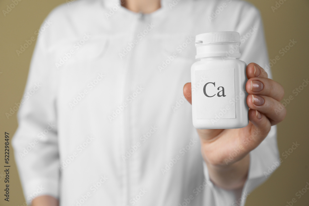 Calcium supplement. Doctor holding bottle with pills on beige background, closeup Calcium supplement. Doctor holding bottle with pills on beige background, closeup