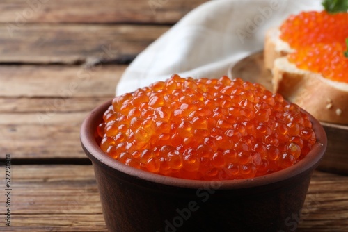 Bowl with delicious red caviar on wooden table, closeup