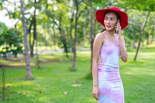 Portrait photo of the beautiful moment of a young asian beautiful lady with red hat happily chatting on her phone with her friends during a garden park strolling