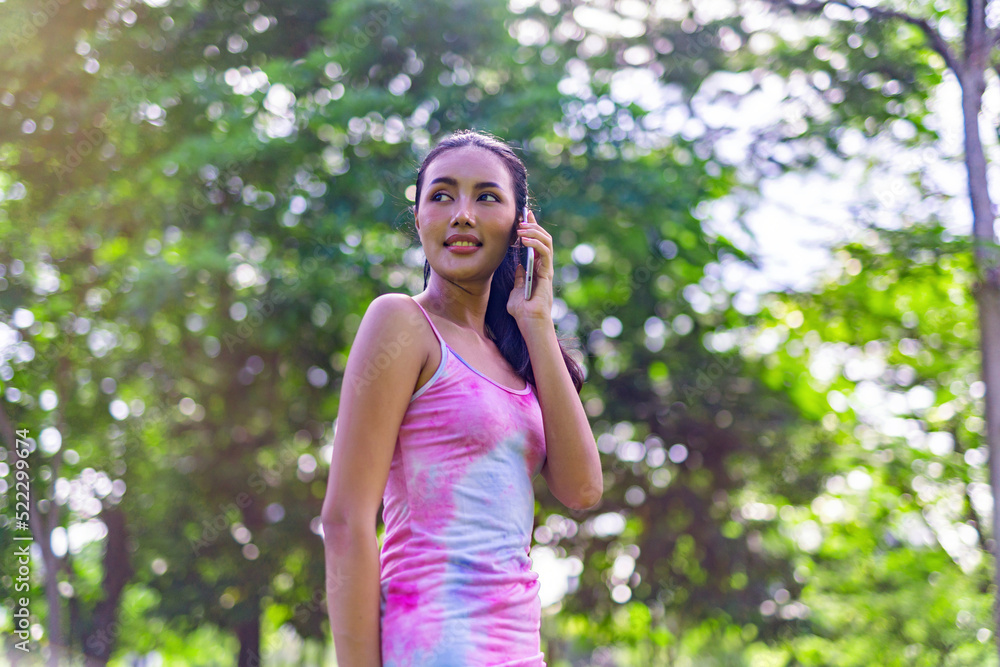 Portrait photo of the beautiful moment of a young asian beautiful lady happily talking on her phone with her friends during a garden park strolling