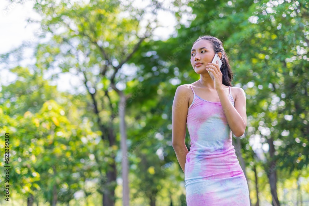 Portrait photo of the beautiful moment of a young asian beautiful lady happily talking on her phone with her friends during a garden park strolling Portrait photo of the beautiful moment of a young asian beautiful lady happily talking on her phone with her friends during a garden park strolling