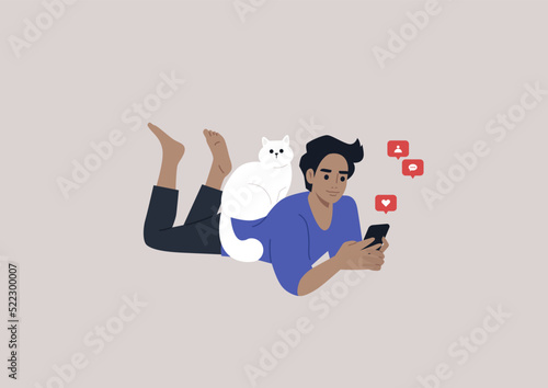 A young male Caucasian character lying on their stomach and checking their mobile phone notifications, a cat sitting on their back