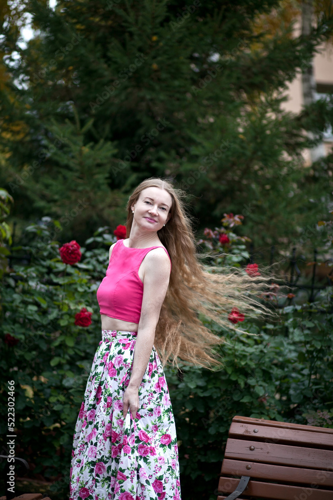 Beautiful woman with long blond hair. A woman walks in a rose garden. Beautiful rose garden. Dress with floral print. Beautiful woman with long blond hair. A woman walks in a rose garden. Beautiful rose garden. Dress with floral print.