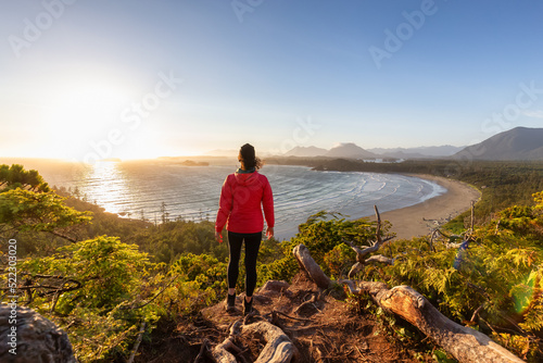 Adventurous Woman Hiker overlooking Sandy Beach on the West Coast of Pacific Ocean. Canadian Nature Landscape Background. Cox Bay Lookout, Tofino, Vancouver Island, BC, Canada.