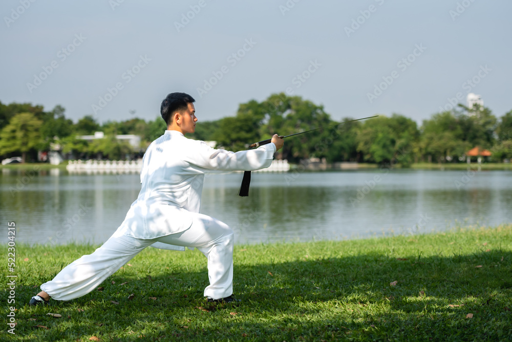Young Asian man doing Tai Chi sword in the park.