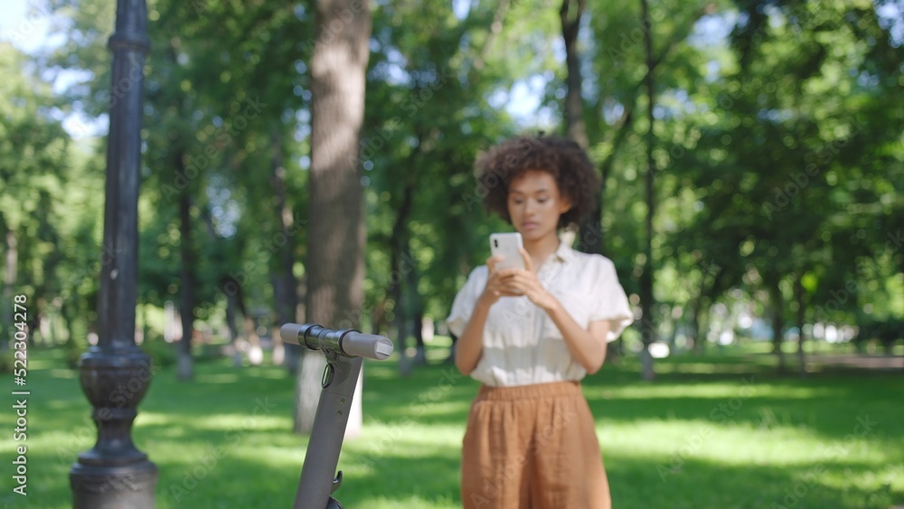 Naklejka premium Young woman finishing her ride on electric scooter, paying on smartphone online