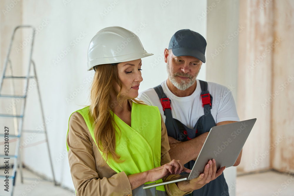 Manager holds open laptop and shows it to builder Manager holds open laptop and shows it to builder