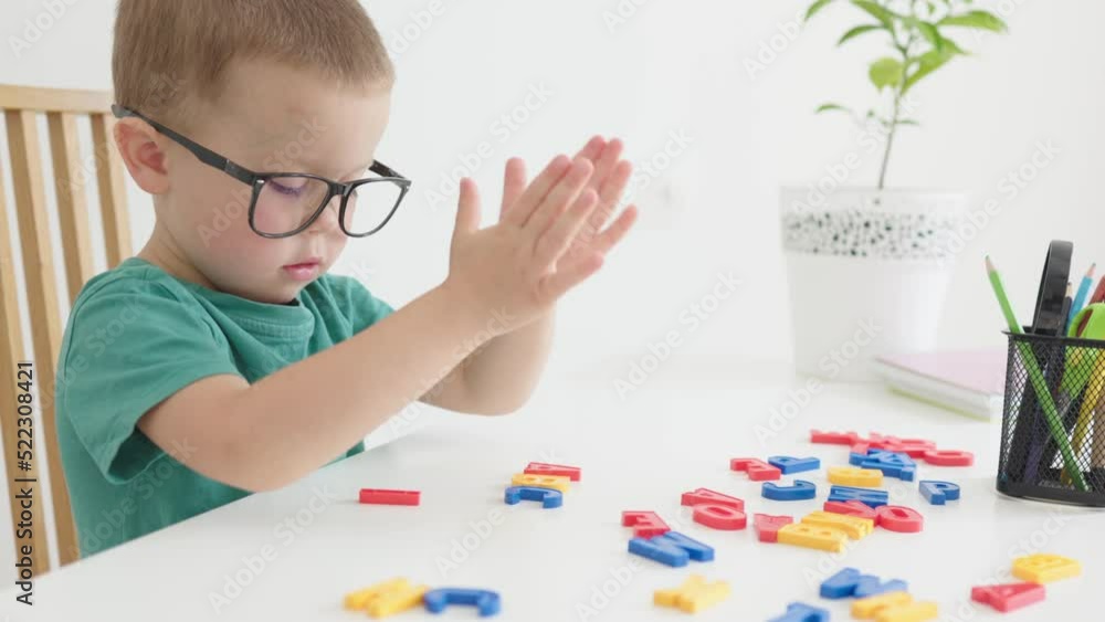 smart baby boy in glasses playing colorful abc alphabetic letters making words. child kid learning to read, early education home schooling concept. cute caucasian preschooler boy sitting at table desk smart baby boy in glasses playing colorful abc alphabetic letters making words. child kid learning to read, early education home schooling concept. cute caucasian preschooler boy sitting at table desk