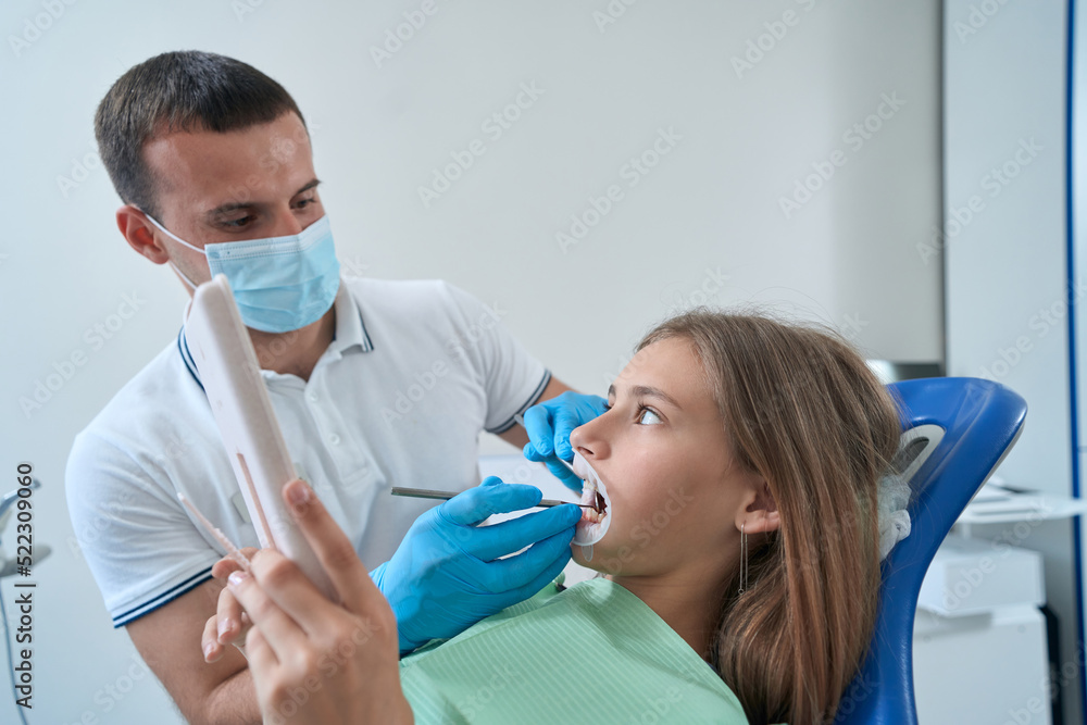 Male doctor checking teeth of adolescent girl Male doctor checking teeth of adolescent girl