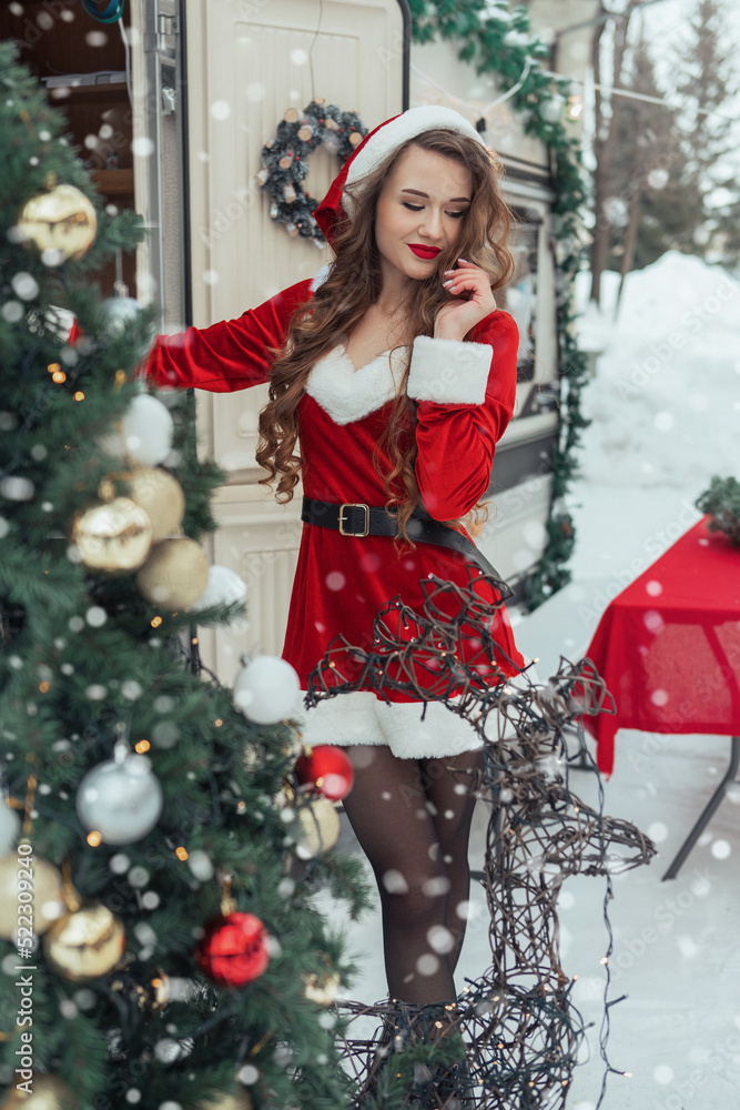 Beauty girl in santa costume decorates the Christmas tree at winter campsite getting ready for the new year. New year celebration concept