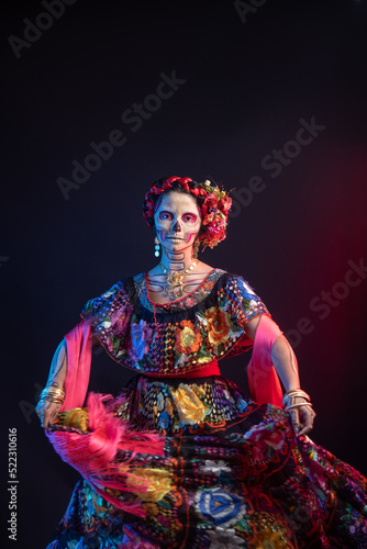 catrina woman dressed in a mexican chiapas costume with a black background pink rebozo and skull and bones makeup on her hands