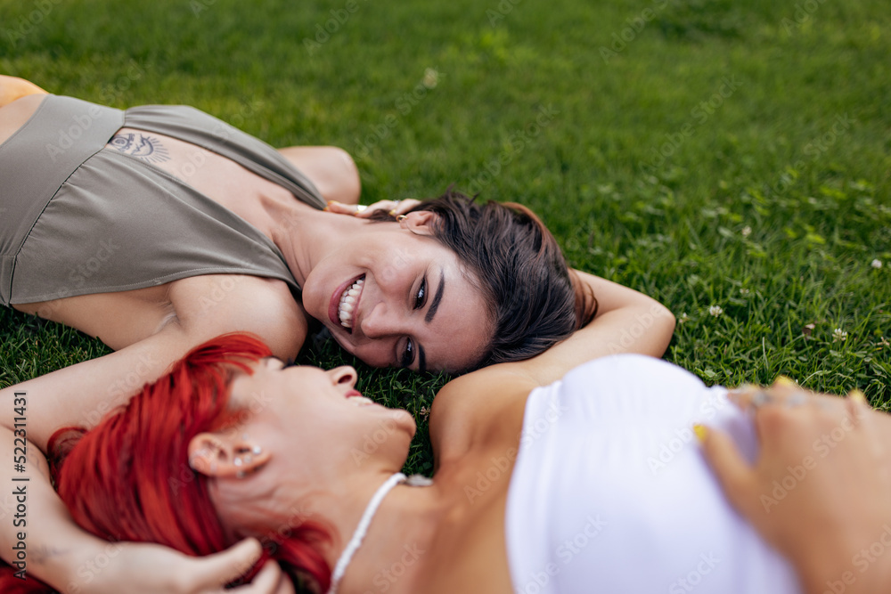 Brunette girl looking at her red-haired girlfriend, laying on the grass. Brunette girl looking at her red-haired girlfriend, laying on the grass.