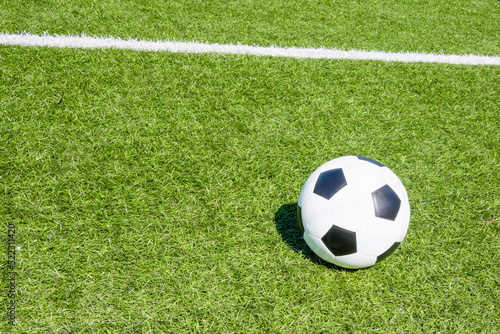 Green artificial turf soccer field with white line  shadow from football goal net and soccer ball on sunny day outdoors. Top view. Football soccer sport background
