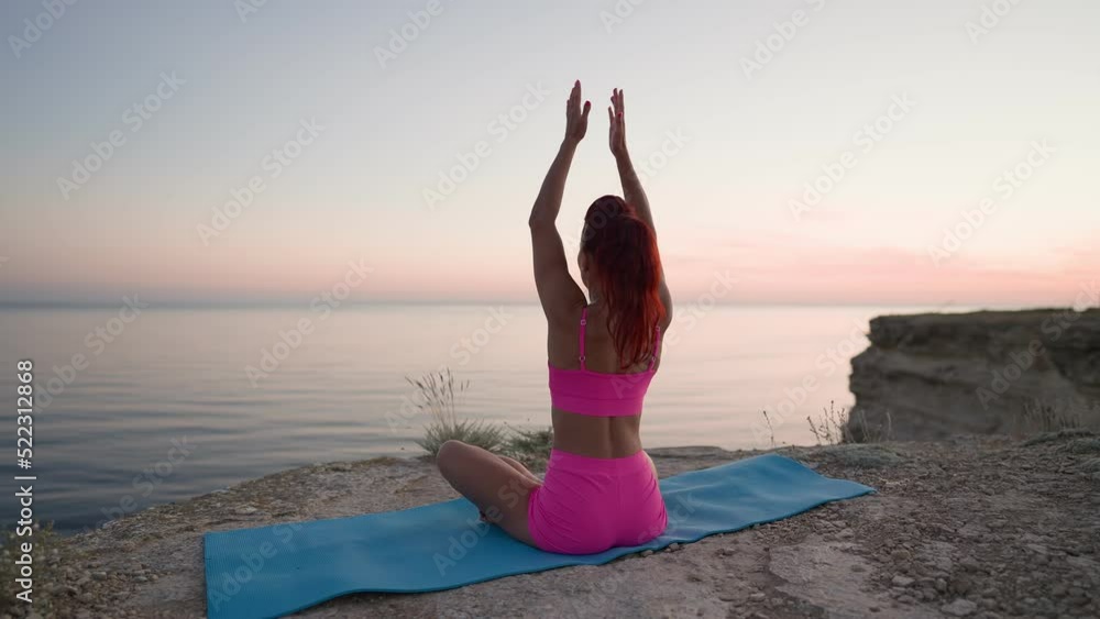 Athletic Fitness Woman in Pink Tank Top and Shorts is Doing Yoga on the Background of Sunset Sea and Rocks. Slim Girl Performs Spiritual Pose and Workout Outdoors. Freedom and Motivation. Slow Motion Athletic Fitness Woman in Pink Tank Top and Shorts is Doing Yoga on the Background of Sunset Sea and Rocks. Slim Girl Performs Spiritual Pose and Workout Outdoors. Freedom and Motivation. Slow Motion