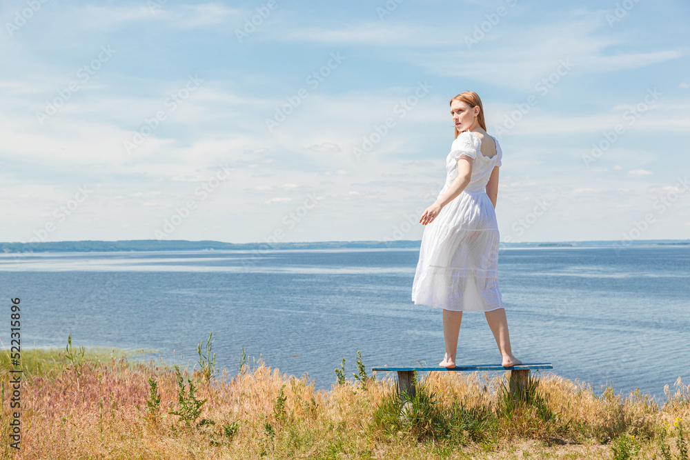 A beautiful girl stands on benches on the seashore with a view of the sky