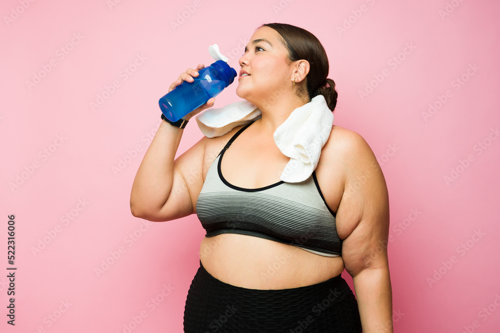 Plus size woman in activewear drinking water during her workout Plus size woman in activewear drinking water during her workout