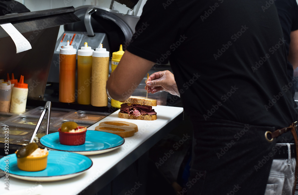 Restaurant kitchen employee working on preparing sandwich for customer food order Restaurant kitchen employee working on preparing sandwich for customer food order
