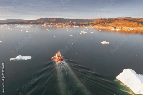 Small ship cruising among ice bergs during beautiful summer day. Disko Bay, Greenland. Climate change and global warming.