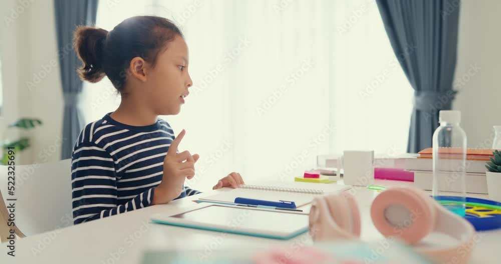 Asian toddler girl with sweater sit in front of desk with notepad use pencil focus on write notebook do homework from online learning course on the weekend at home. Distance online learning concept. Asian toddler girl with sweater sit in front of desk with notepad use pencil focus on write notebook do homework from online learning course on the weekend at home. Distance online learning concept.
