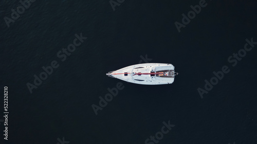 Top air view on small white yacht floating in the sea in evening.