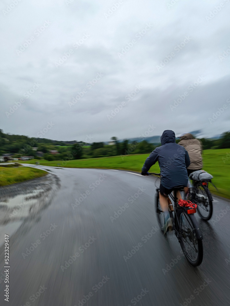 Obraz premium Two cycling male tourists moving rapidly on Norway fjords coastal road 6