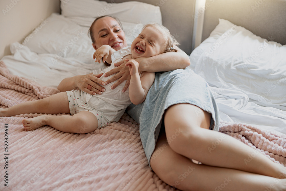 Young mother smiling and playing with her baby while lying in bed at home Young mother smiling and playing with her baby while lying in bed at home