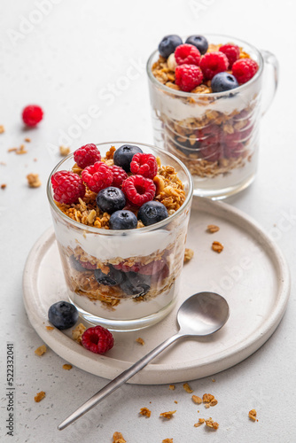 Granola with yogurt in glass served with fresh raspberry, blueberry and honey. Homemade oatmeal muesli. Vegetarian breakfast, healthy eating concept. Selective focus.