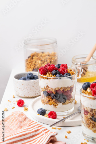 Granola with yogurt in glass served with fresh raspberry, blueberry and honey. Homemade oatmeal muesli. Vegetarian breakfast, healthy eating concept. Selective focus.