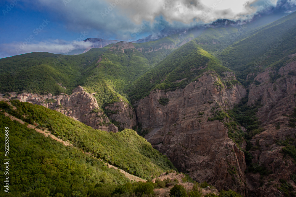 Fototapeta premium Mountain Peaks Trapping Light entangled Smoky Clouds Letting few Sunrays shine on The Trees Covering The Cliffs Creating A Breathtaking Landscape Scenic View