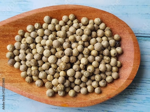 White peppercorns (Piper nigrum), in a wooden spoon, isolated on a wooden table, top view. photo