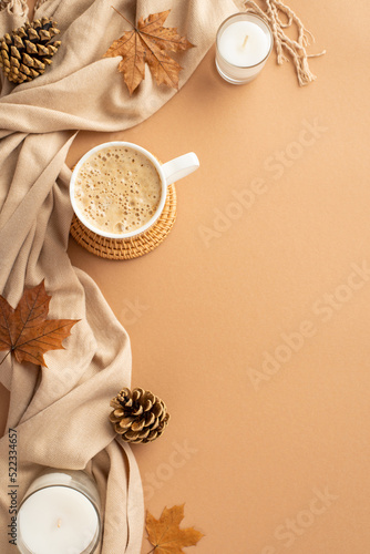 Autumn business concept. Top view vertical photo of cup of frothy coffee on rattan serving mat fallen maple leaves pine cones candles and plaid on isolated beige background