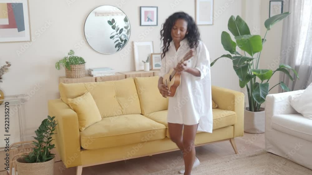 African American young woman happily playing ukulele in modern apartment. Domestic life African American young woman happily playing ukulele in modern apartment. Domestic life