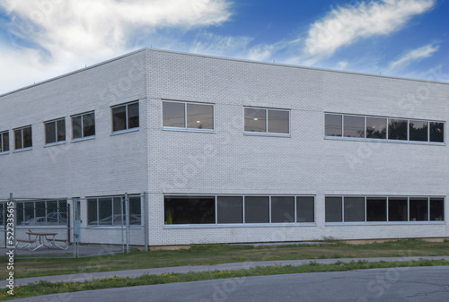 Exterior corner of nondescript two story white brick office or factory building during daytime, chain link fence, picnic table, nobody