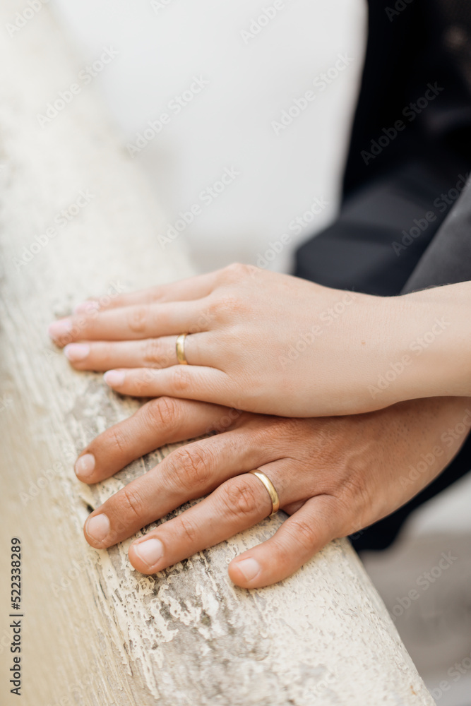Cropped photo of hands of loving couple with wedding rings. Brides hand covering grooms hand on white railing. Wedding. Cropped photo of hands of loving couple with wedding rings. Brides hand covering grooms hand on white railing. Wedding.