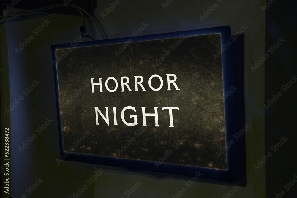 A flat TV set mounted on the wall of a room, showing the intertitle from an old silent film with the text Horror Night. Angled shot.

