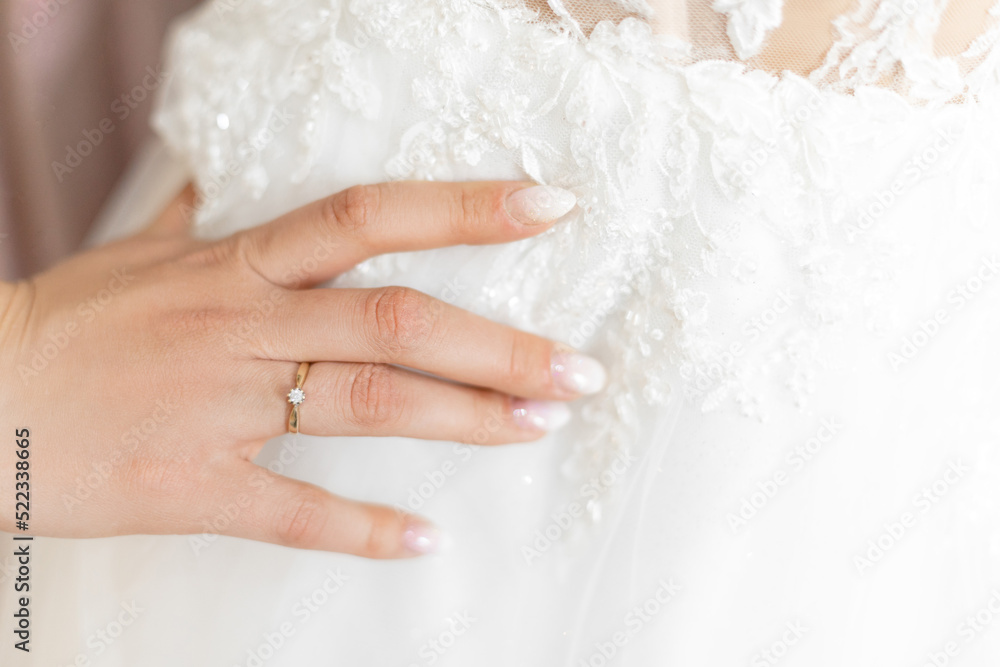 Cropped photo of woman touching white wedding embroidered dress with tender floral patterns with hand with white nails. Cropped photo of woman touching white wedding embroidered dress with tender floral patterns with hand with white nails.