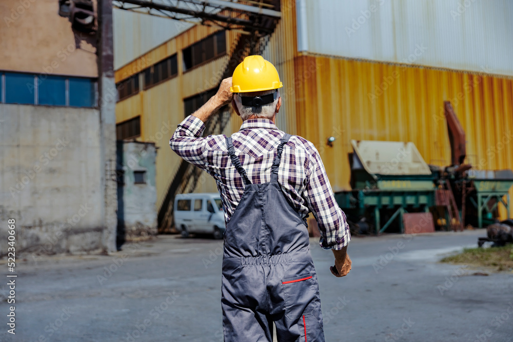 Factory worker going to his workplace. A senior factory worker puts the helmet on his head and walks to his workplace. Factory worker going to his workplace. A senior factory worker puts the helmet on his head and walks to his workplace.