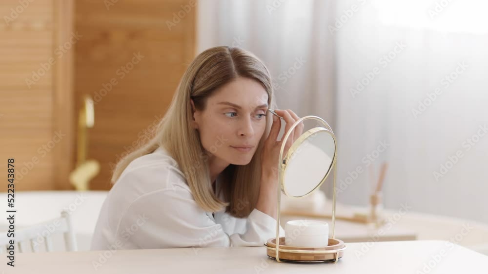 Domestic grooming concept. Beautiful middle aged woman wearing silk bathrobe plucking eyebrows herself, empty space Domestic grooming concept. Beautiful middle aged woman wearing silk bathrobe plucking eyebrows herself, empty space