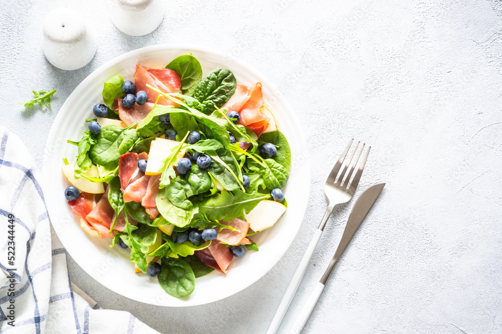Healthy salad with spinach, jamon, pear and blueberry. Top view on white background with space for text. Healthy salad with spinach, jamon, pear and blueberry. Top view on white background with space for text.