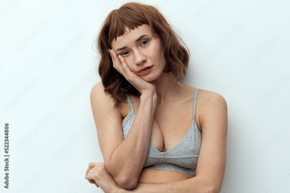 a sweet, thoughtful woman with red hair stands against a light background and poses relaxed touching her face with her hand. Studio photo with an empty space for inserting an advertising layout a sweet, thoughtful woman with red hair stands against a light background and poses relaxed touching her face with her hand. Studio photo with an empty space for inserting an advertising layout