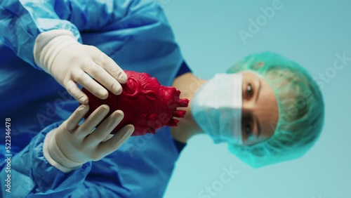 young caucasian surgeon holding a 3d artifficial heart model and showing it to the camera, cardiovascular diseases prevention vertical shot. High quality 4k footage photo