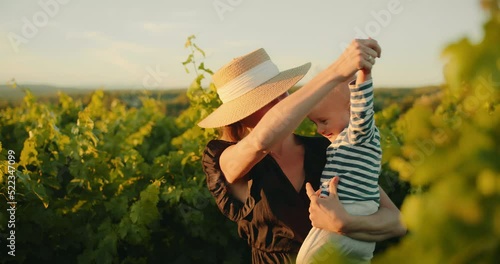 Young beautiful female in dress having good time with her little kid in summer vineyard of Provence during sunset. Young family enjoying time together. Happy childhood and motherhood concept. 