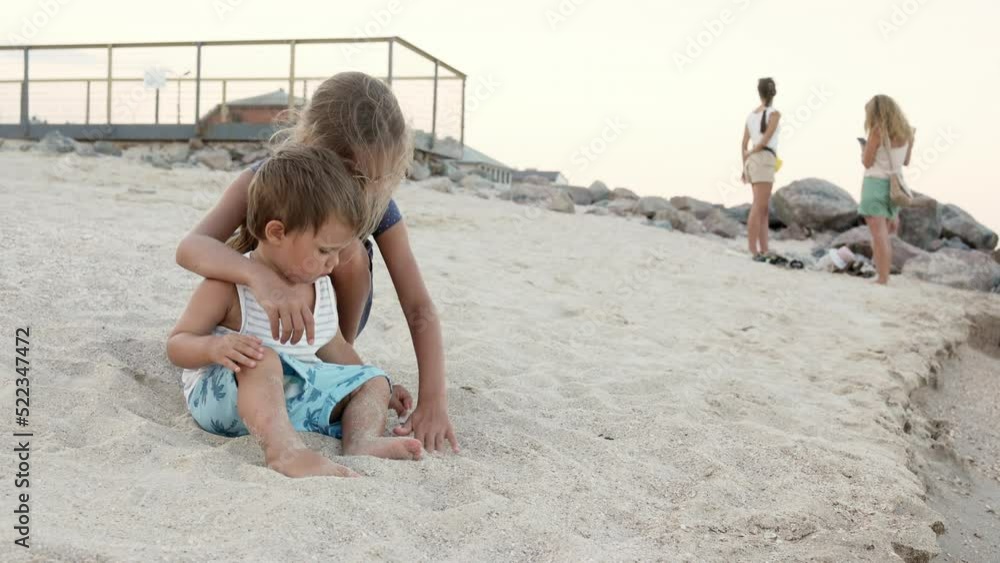 Girl helping her little brother to look for seashells in the sand on the coast Girl helping her little brother to look for seashells in the sand on the coast