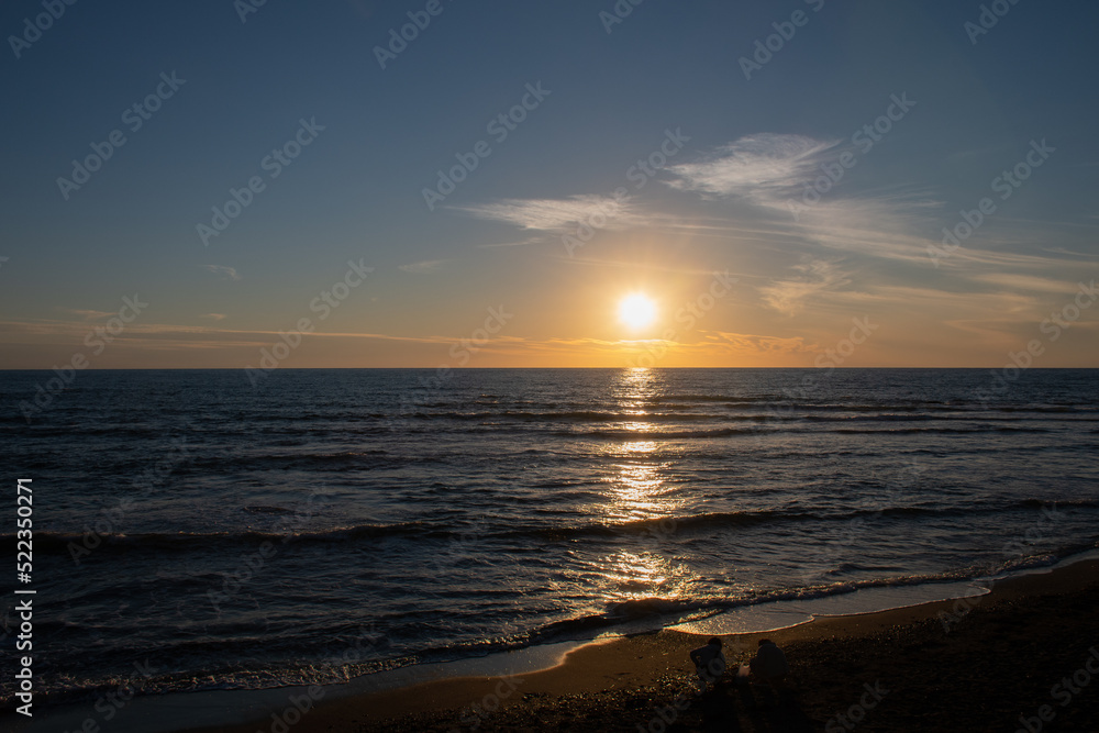 水平線に沈む夕陽と砂浜で遊ぶ人
