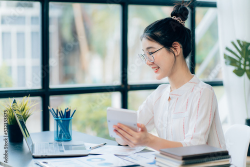 Portraits of beautiful smiling Asian women relax using laptop computer technology while sitting on their desks and using their creativity to work