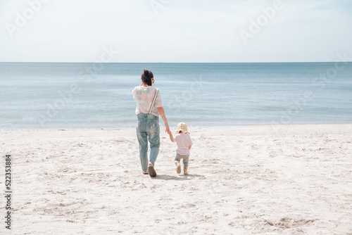 On the beach, a mother and her daughter walk hand in hand.