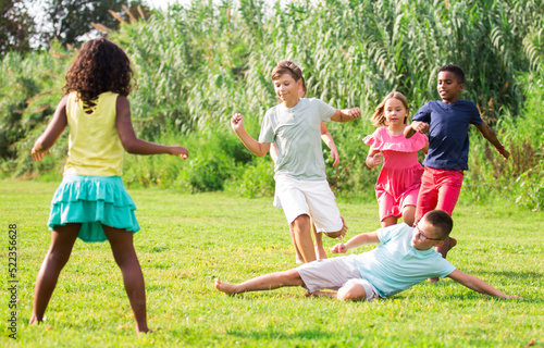 International group of active tweenagers having fun together outdoors, playing football on green grass in summertime