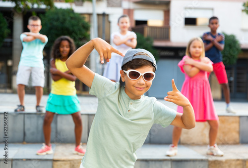 Modern preteen boy krump dancer in sunglasses posing during performance with group of tweens on summer city street.. photo