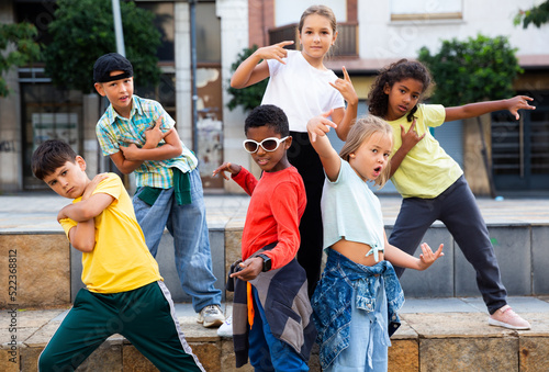 International group of modern tweenagers performing street dance choreography outdoors in summer.