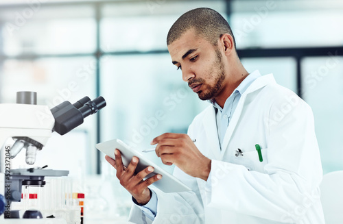 Photo Serious male scientist working on a tablet reviewing an online phd publication in a lab